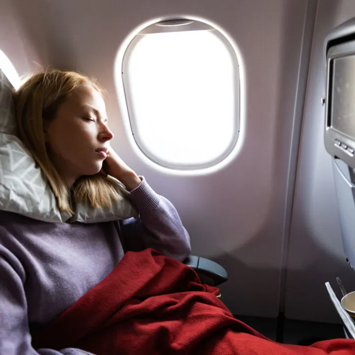 Woman sleeping on a plane with a red blanket.