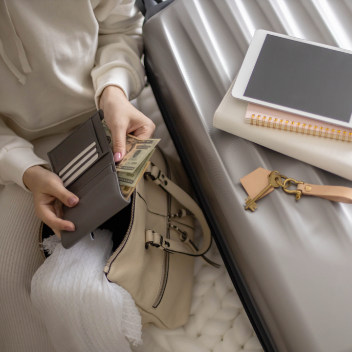 woman sitting on a bed with luggage and a wallet.