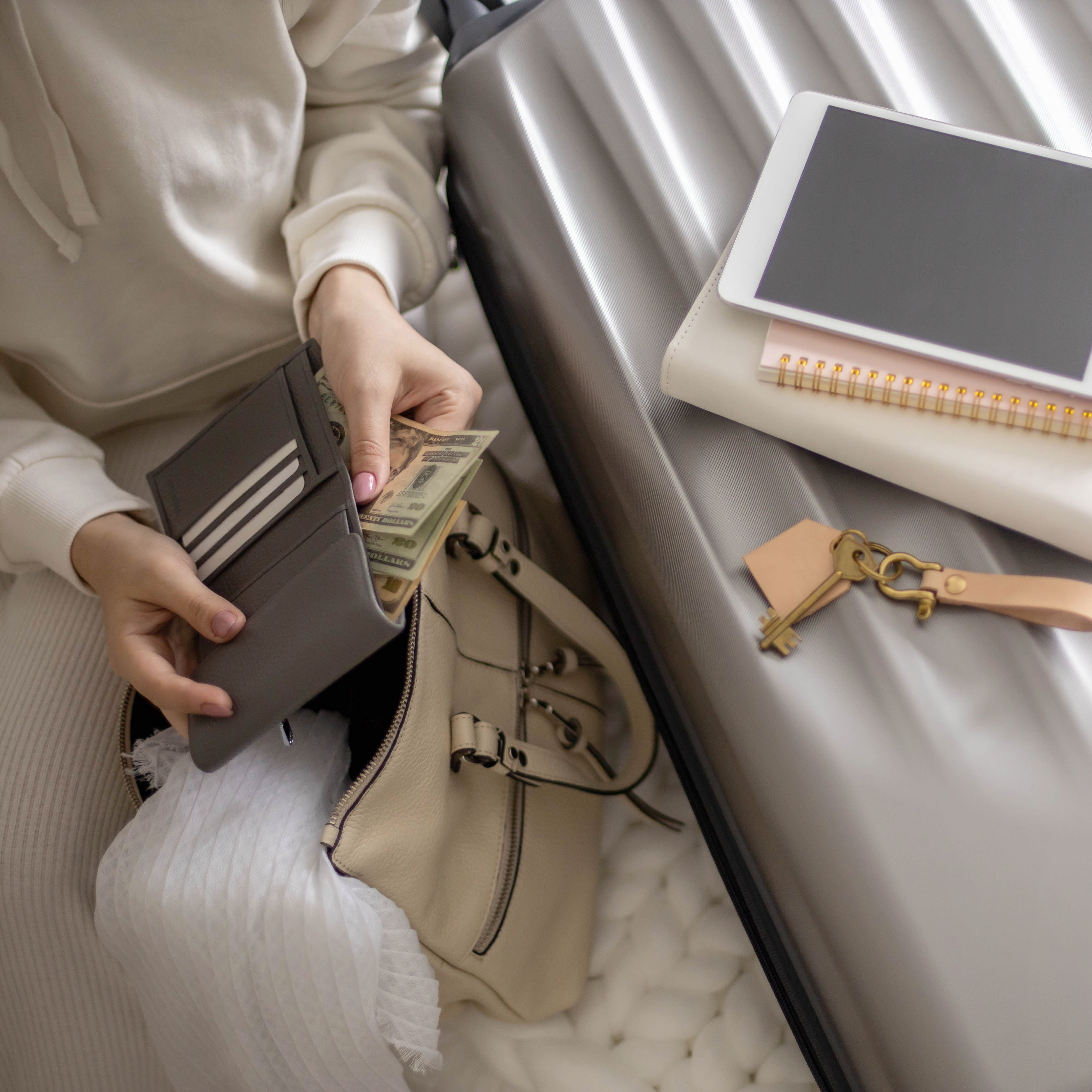 Woman sitting on a bed with luggage and a wallet.