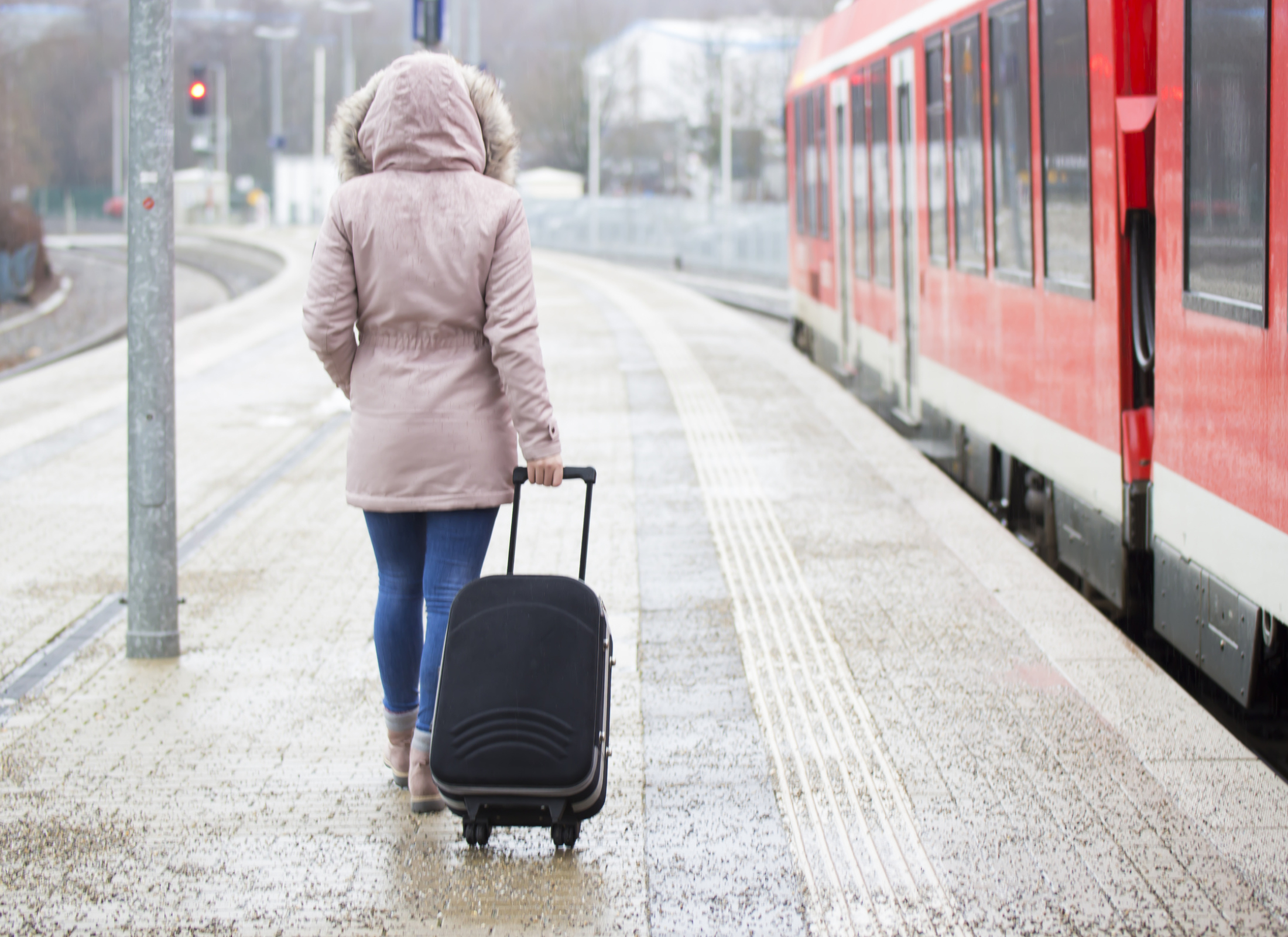 Woman rolls luggage in a wintery train station platform.