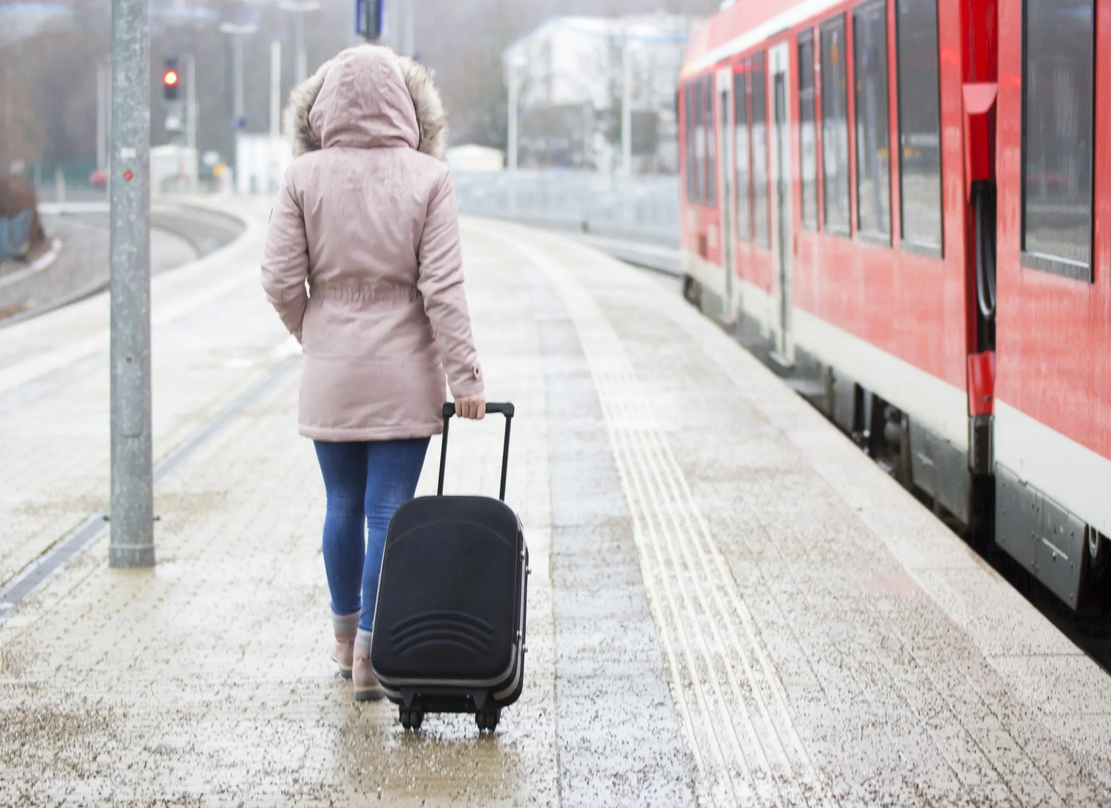 Woman rolls luggage in a wintery train station platform.