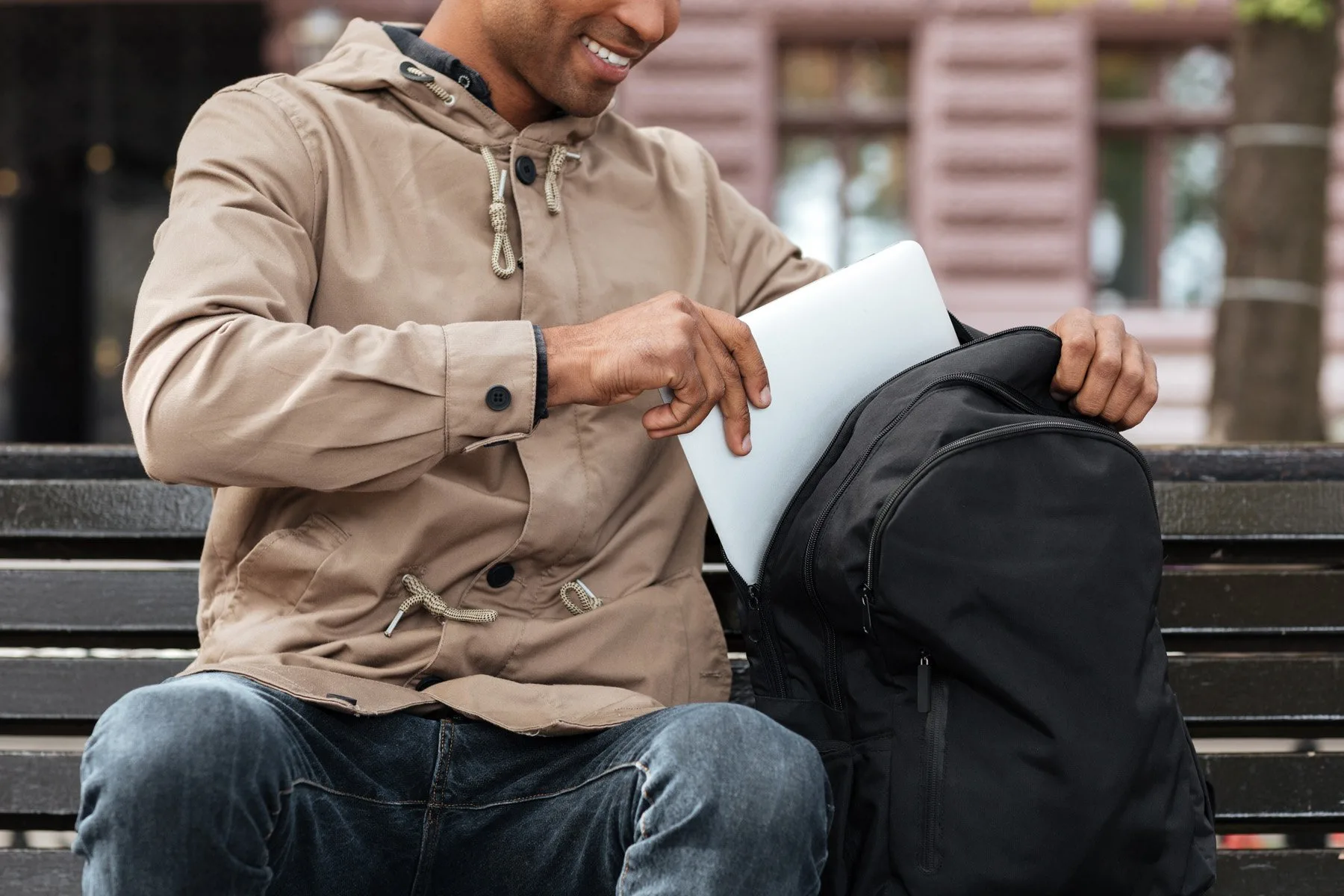 Cropped photo of young cheerful african man getting laptop from the backpack.