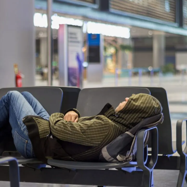 a person sleeps on plastic chairs at an airport.