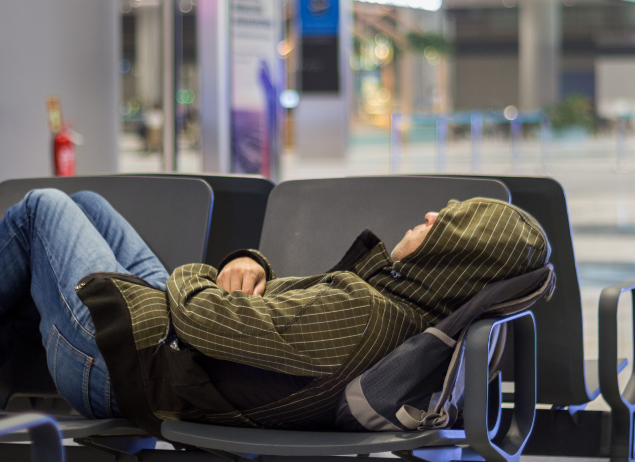 A person sleeps on plastic chairs at an airport during a long layover.
