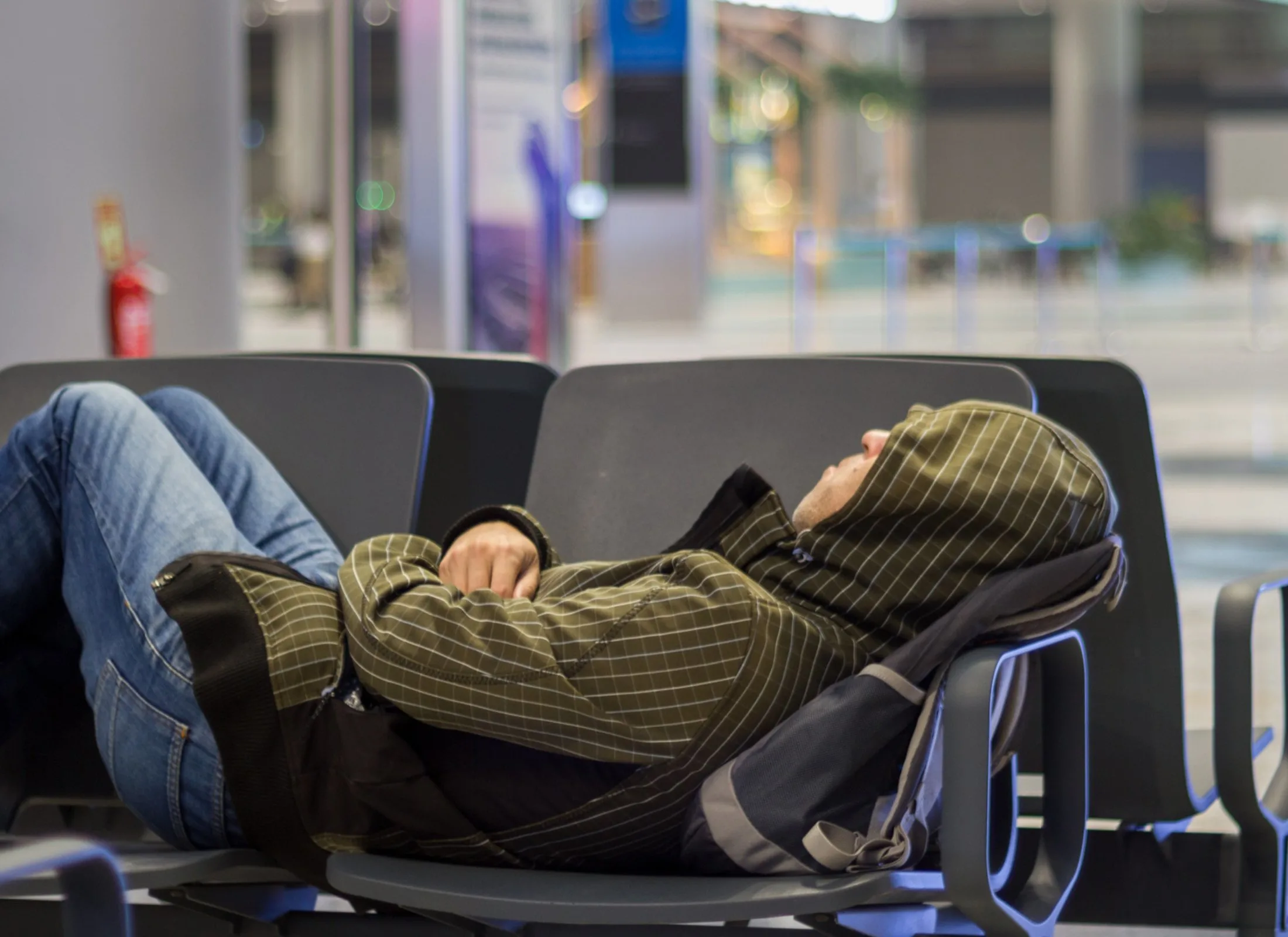 A person sleeps on plastic chairs at an airport during a long layover.