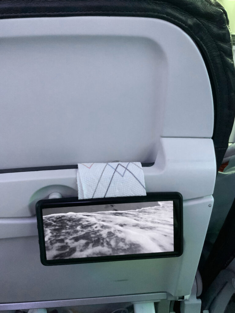 A cell phone mounted on the tray table on back of an airline seat for easy viewing.