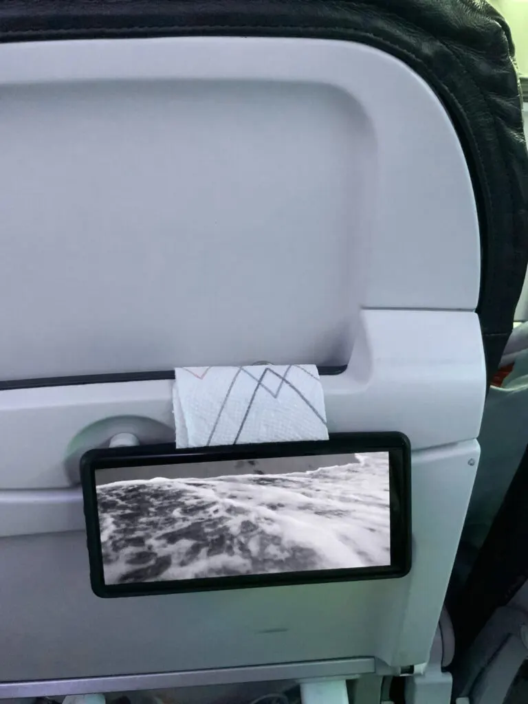 A cell phone mounted on the tray table on back of an airline seat for easy viewing.
