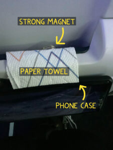 A cell phone mounted on the tray table on back of an airline seat for easy viewing.