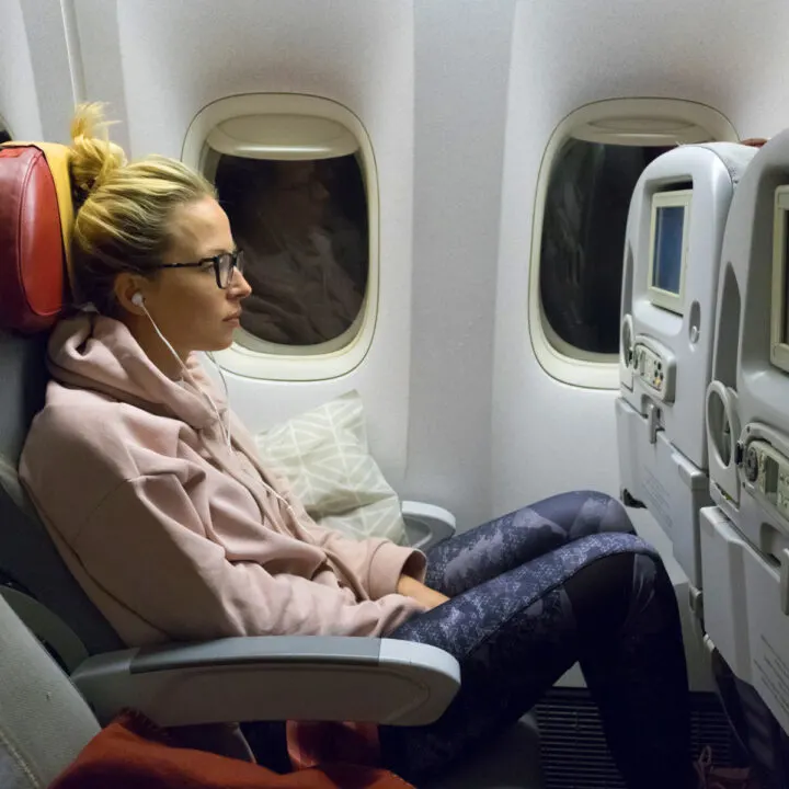 Sporty casual young blonde caucasian lady watching movie while traveling by airplane by the window. Commercial transportation by planes.