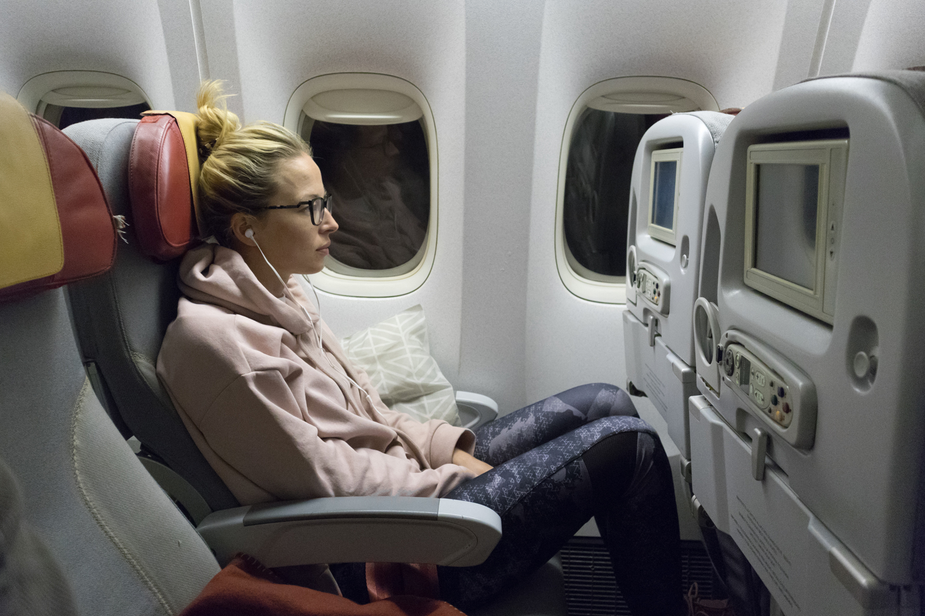 Sporty casual young blonde caucasian lady watching movie while traveling on a long flight.