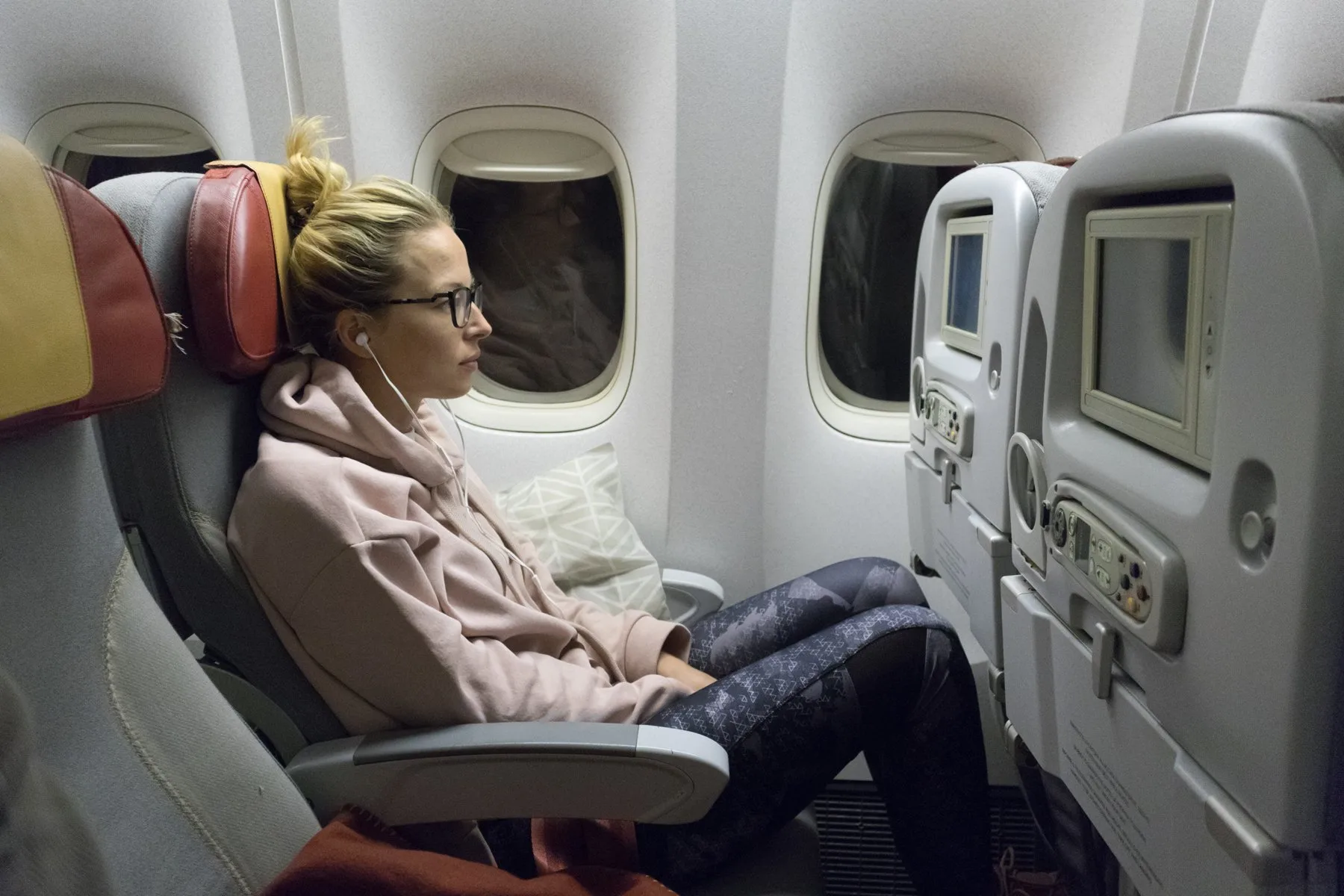 Sporty casual young blonde caucasian lady watching movie while traveling on a long flight.