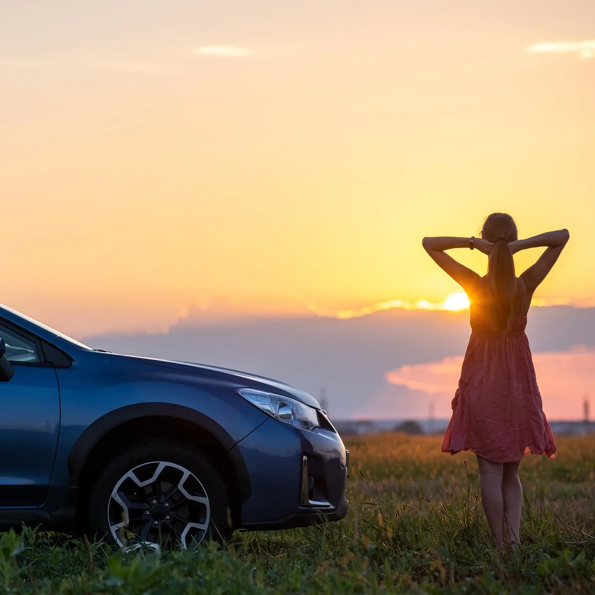 Dark silhouette of woman driver standing near her car on grassy field enjoying view of bright sunset. Young female relaxing during road trip beside suv vehicle.