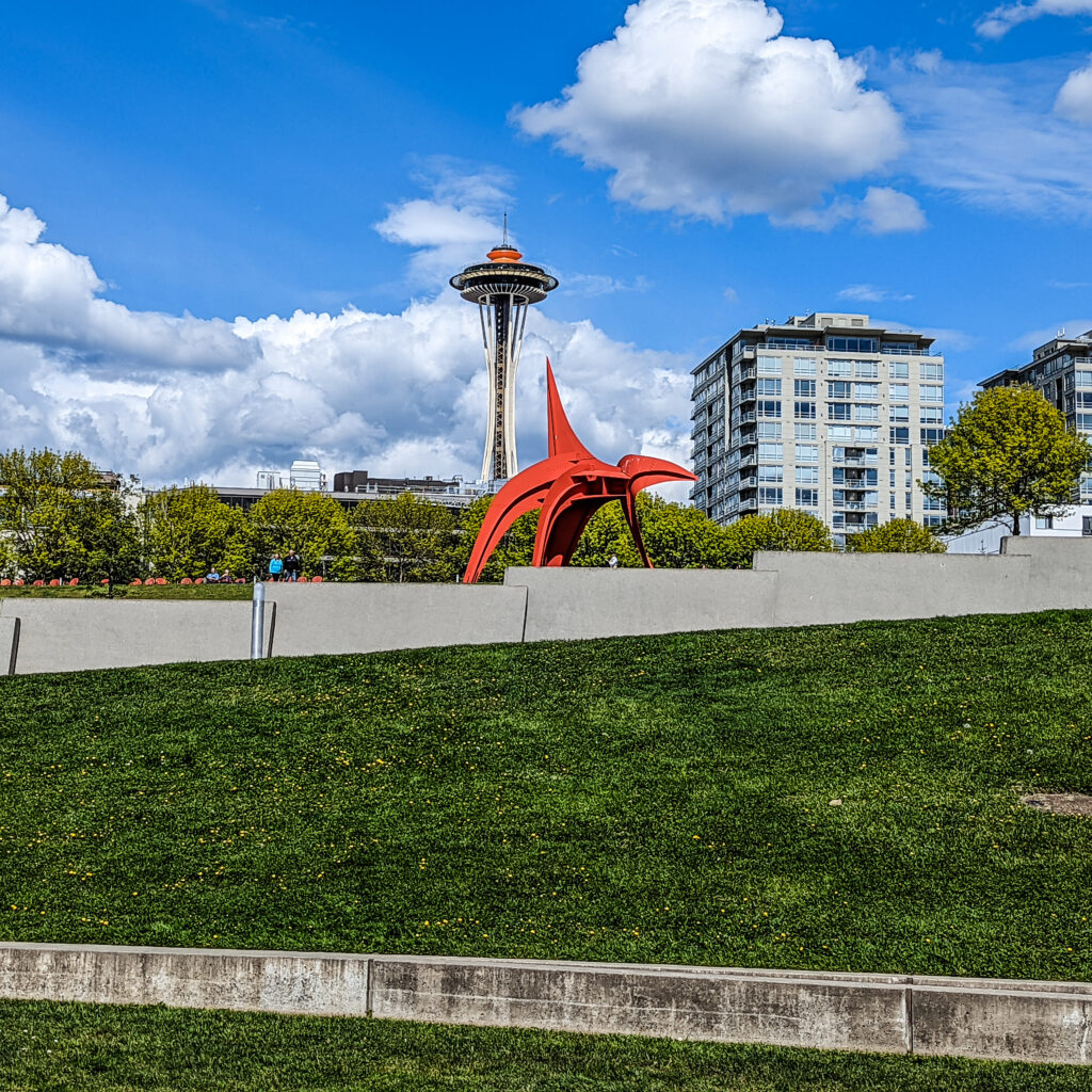 A calder sculpture in the olympic sculpture park is shown in the foreground with the space needle in the background.