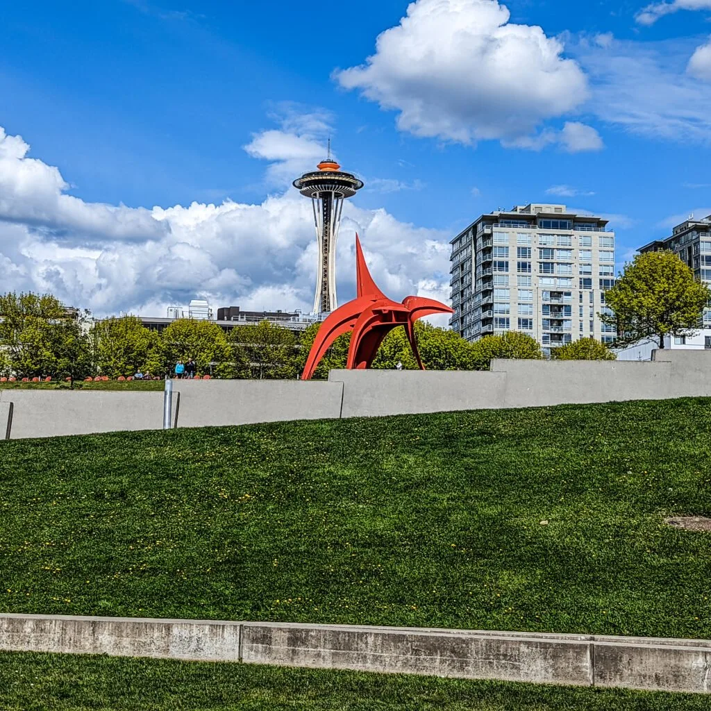 A calder sculpture in the olympic sculpture park is shown in the foreground with the space needle in the background.