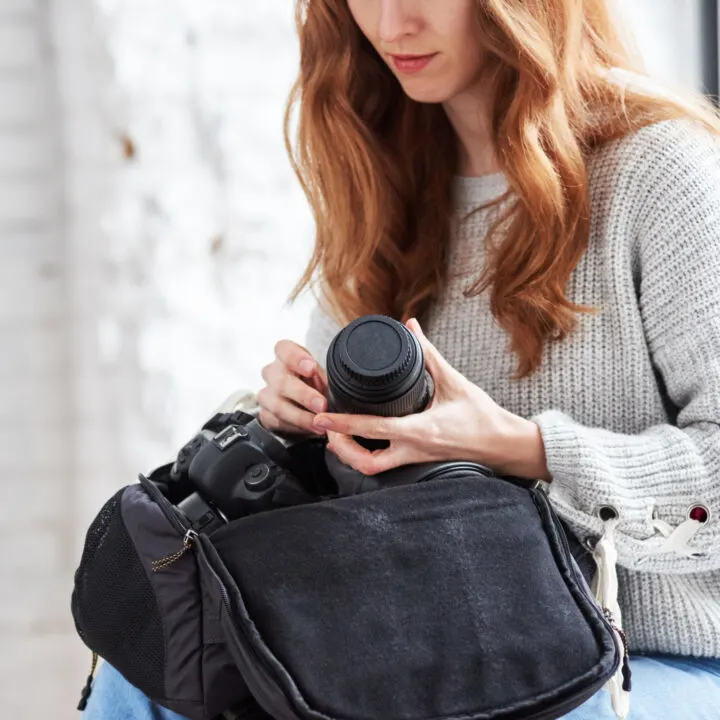 A woman holds a professional expensive camera and a travel camera bag