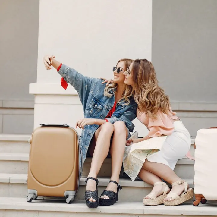 Two friends with luggage posing for a photograph.