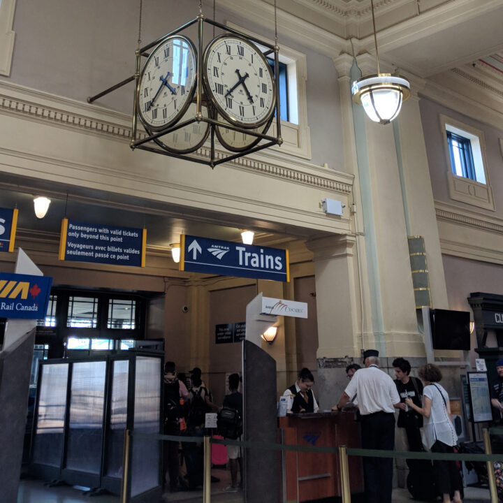 A large clock hangs in a train station above a sign for Amtrak trains.