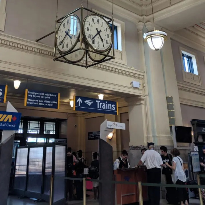 A large clock hangs in a train station above a sign for Amtrak trains.