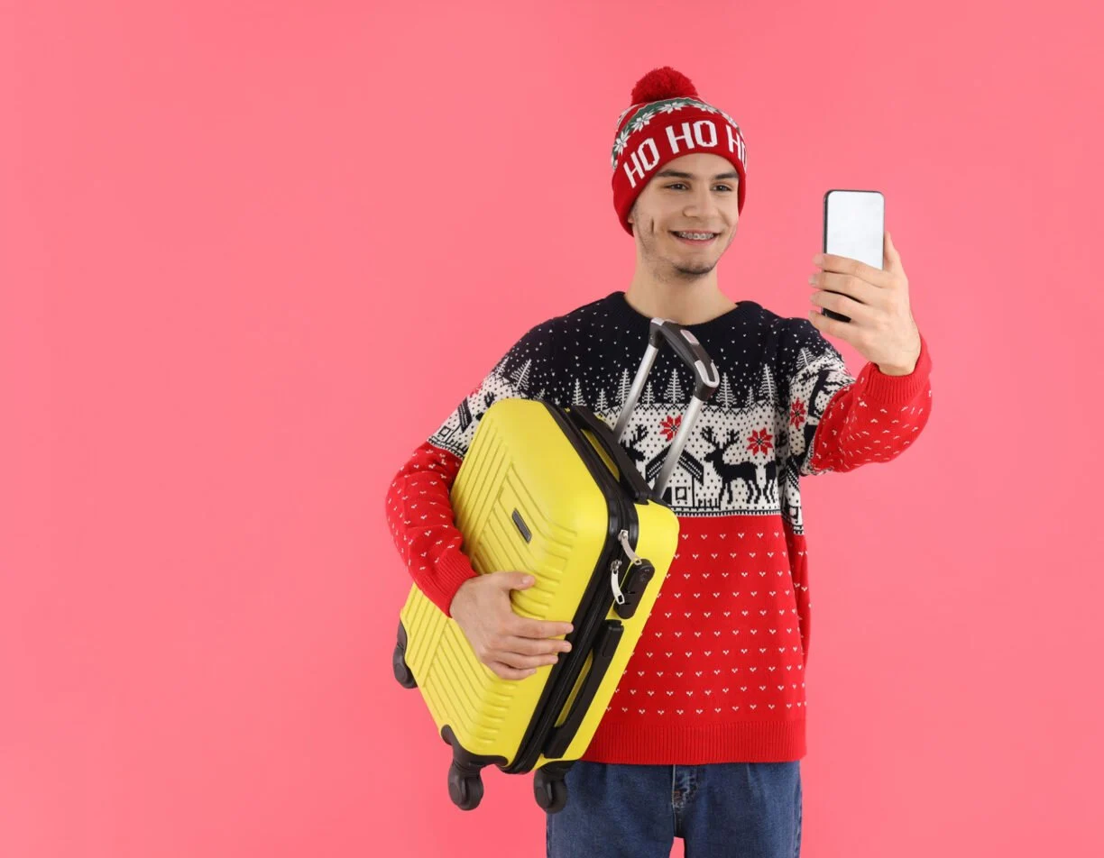 A man clicking a selfie in christmas attire with luggage in hand.