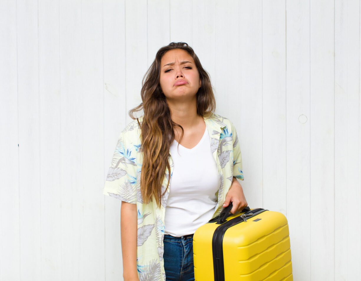A frowning girl with luggage in hand.