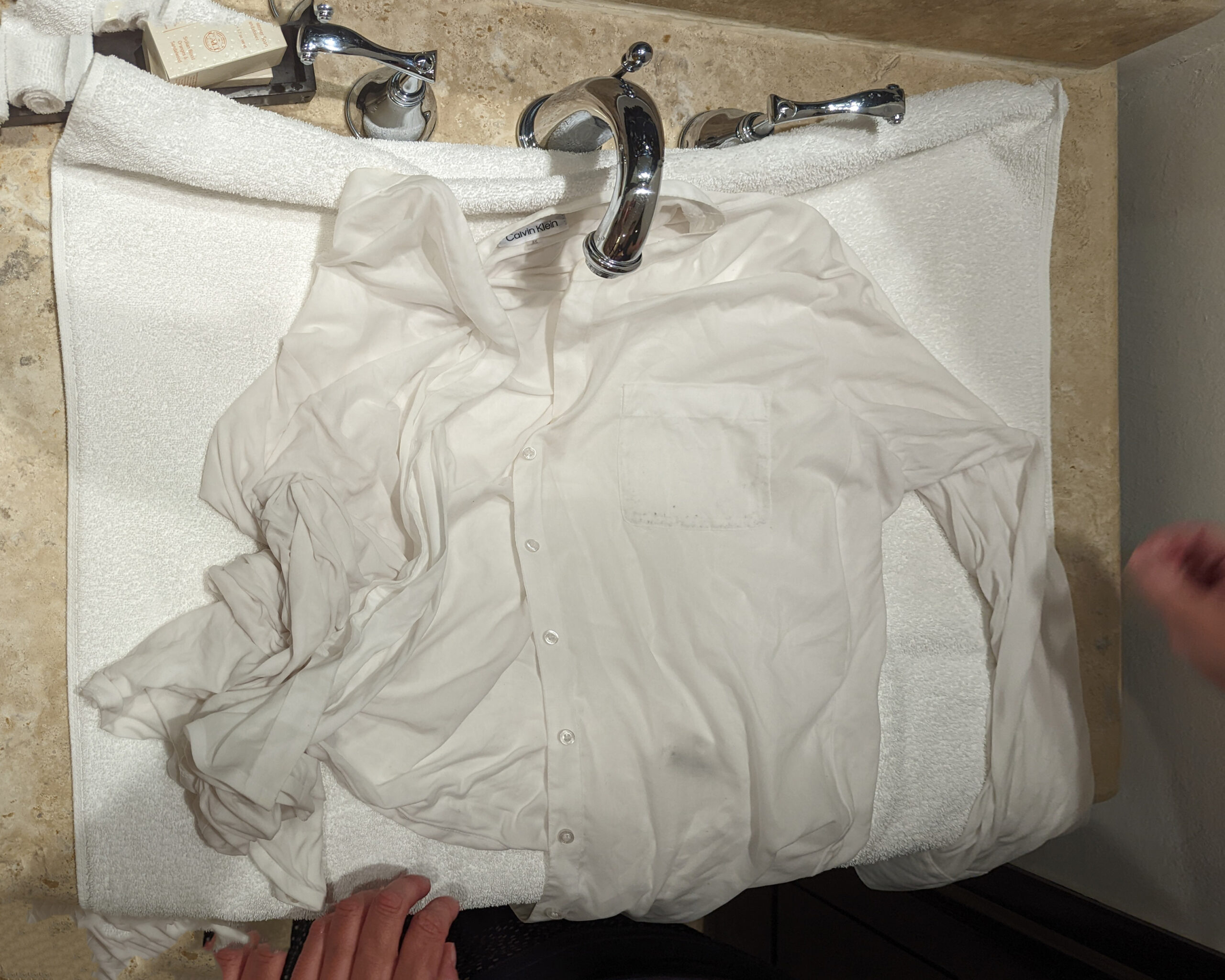 Hands squeezing water out of a white shirt over a hotel sink.