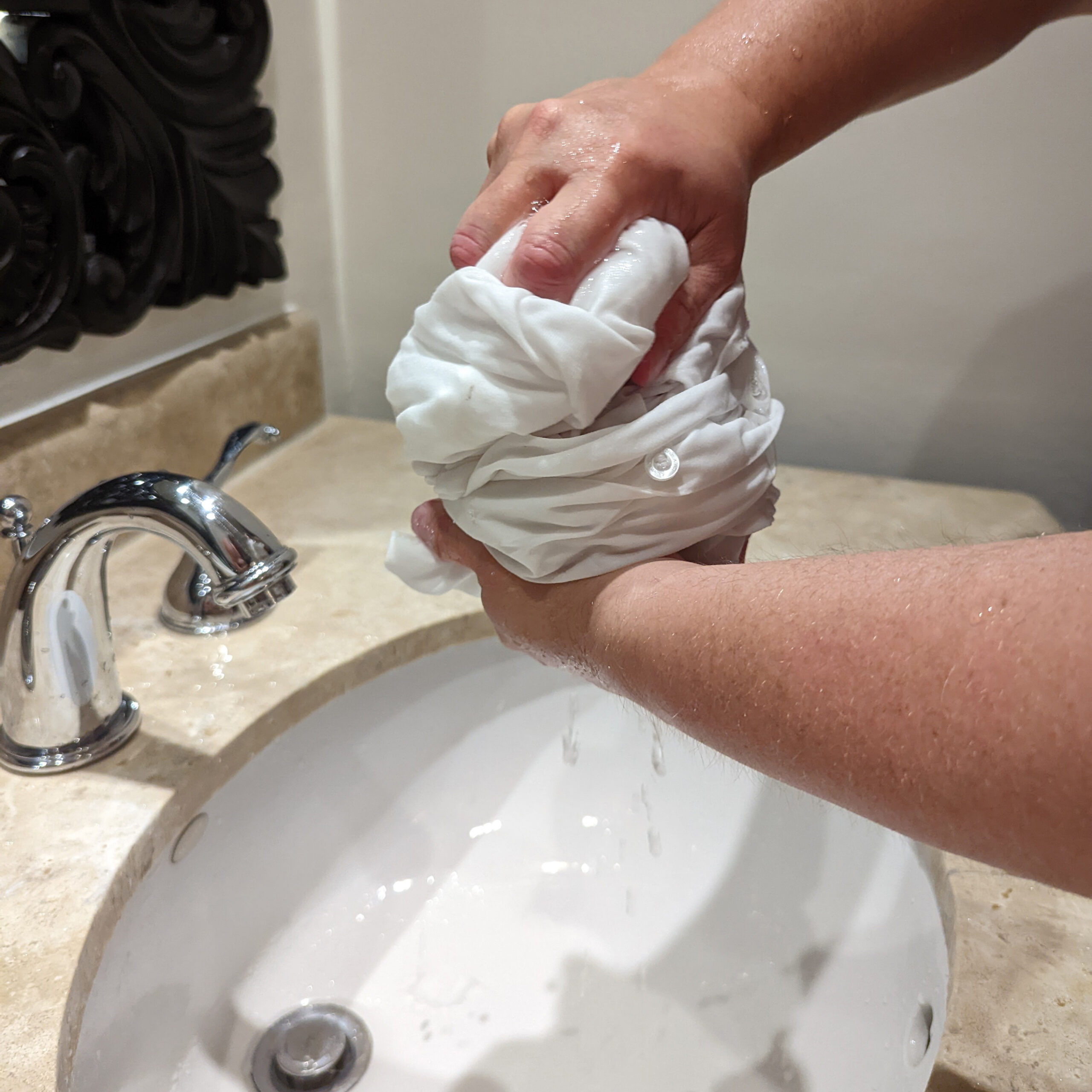 Hands squeezing water out of a white shirt over a hotel sink.