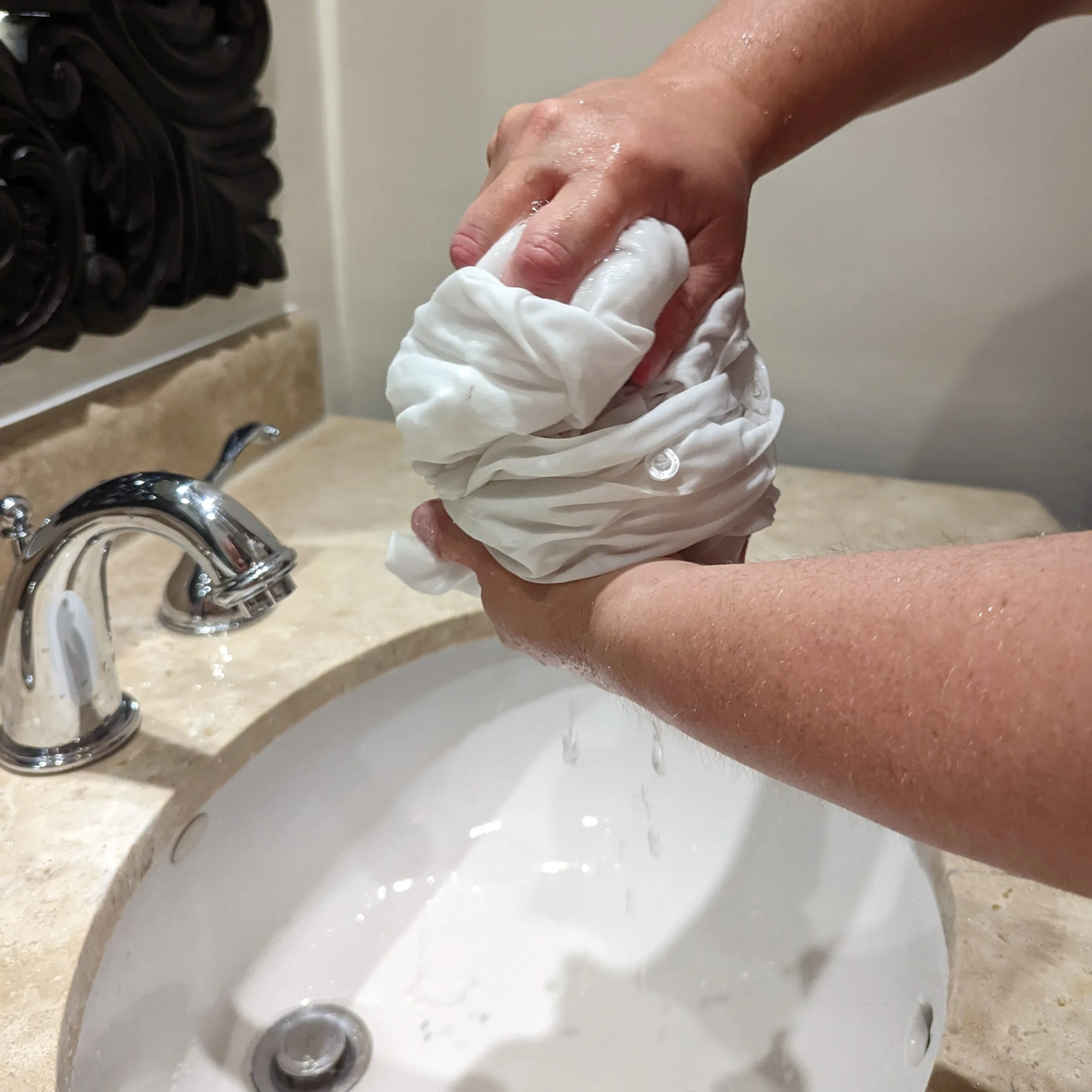 Hands squeezing water out of a white shirt over a hotel sink.