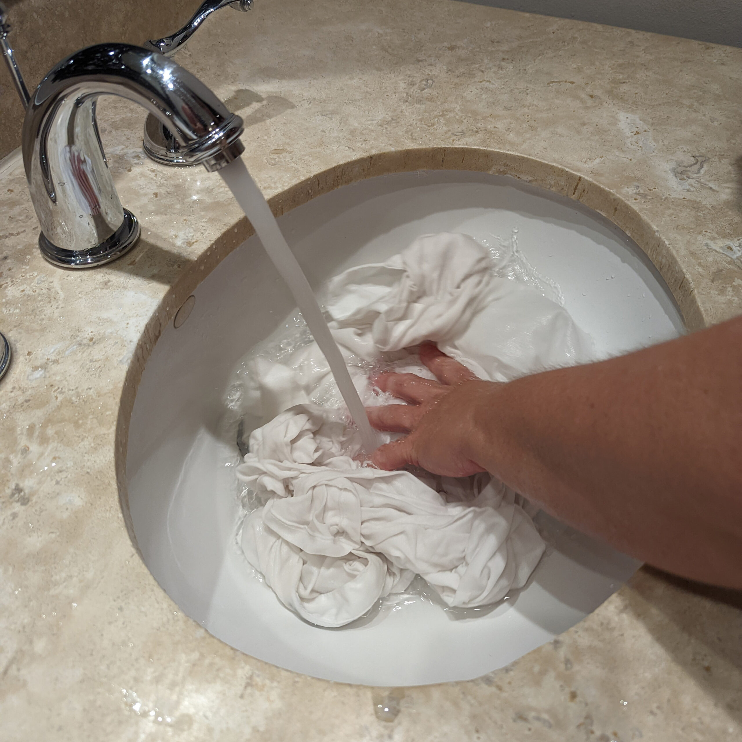 Hands rinsing white shirt in a hotel sink.