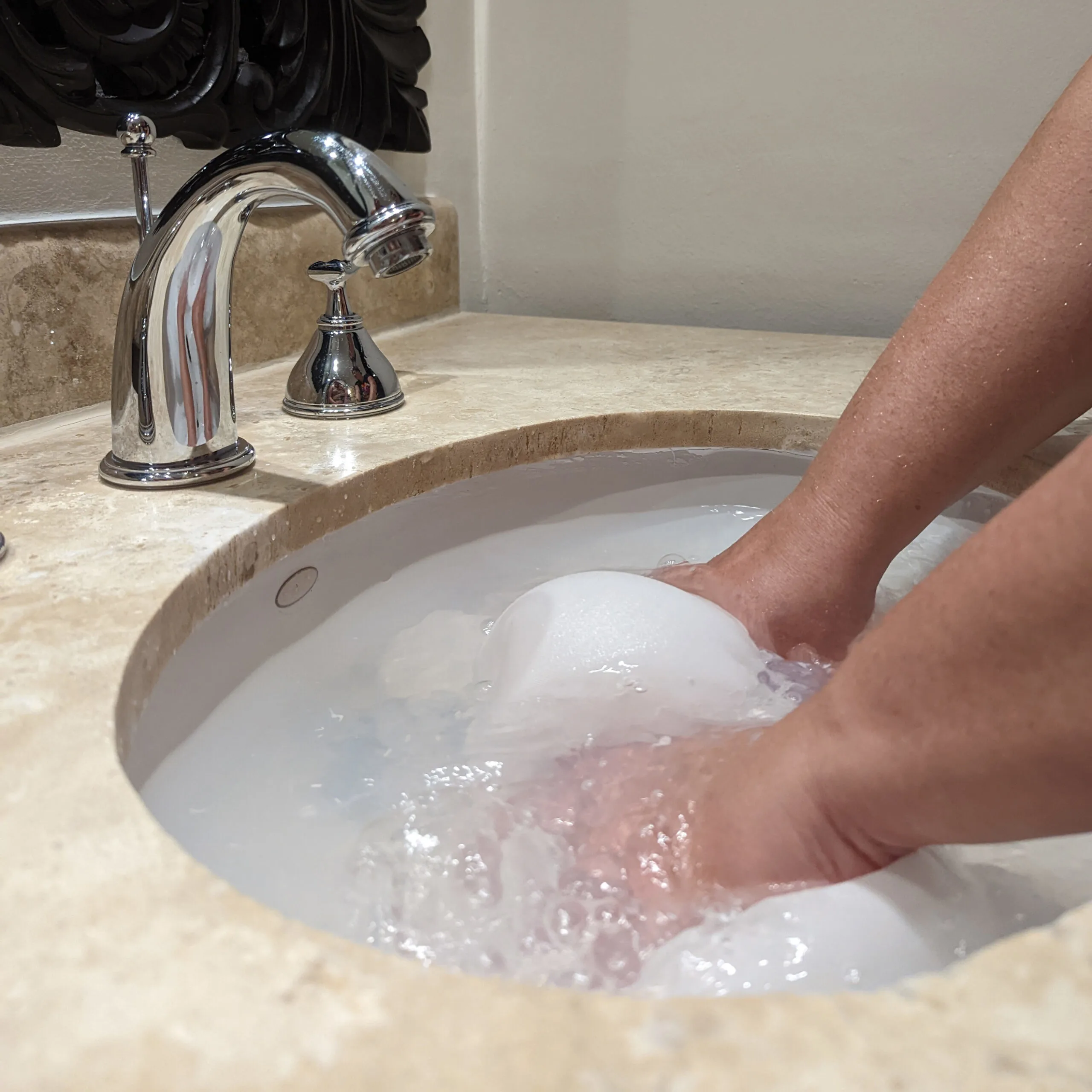 Hands soaking a white shirt in a hotel sink.