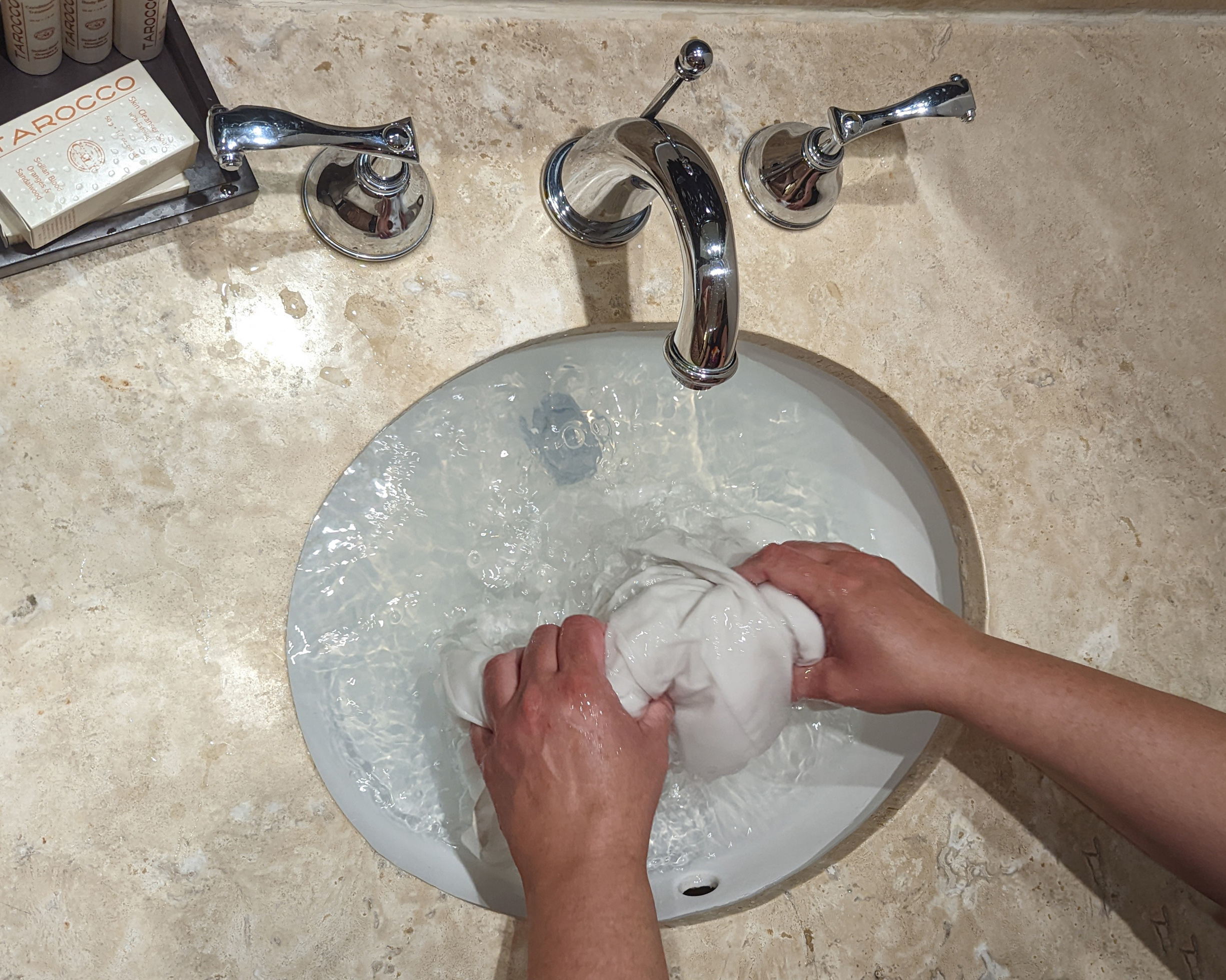 Hands scrubbing a white shirt in a hotel sink.