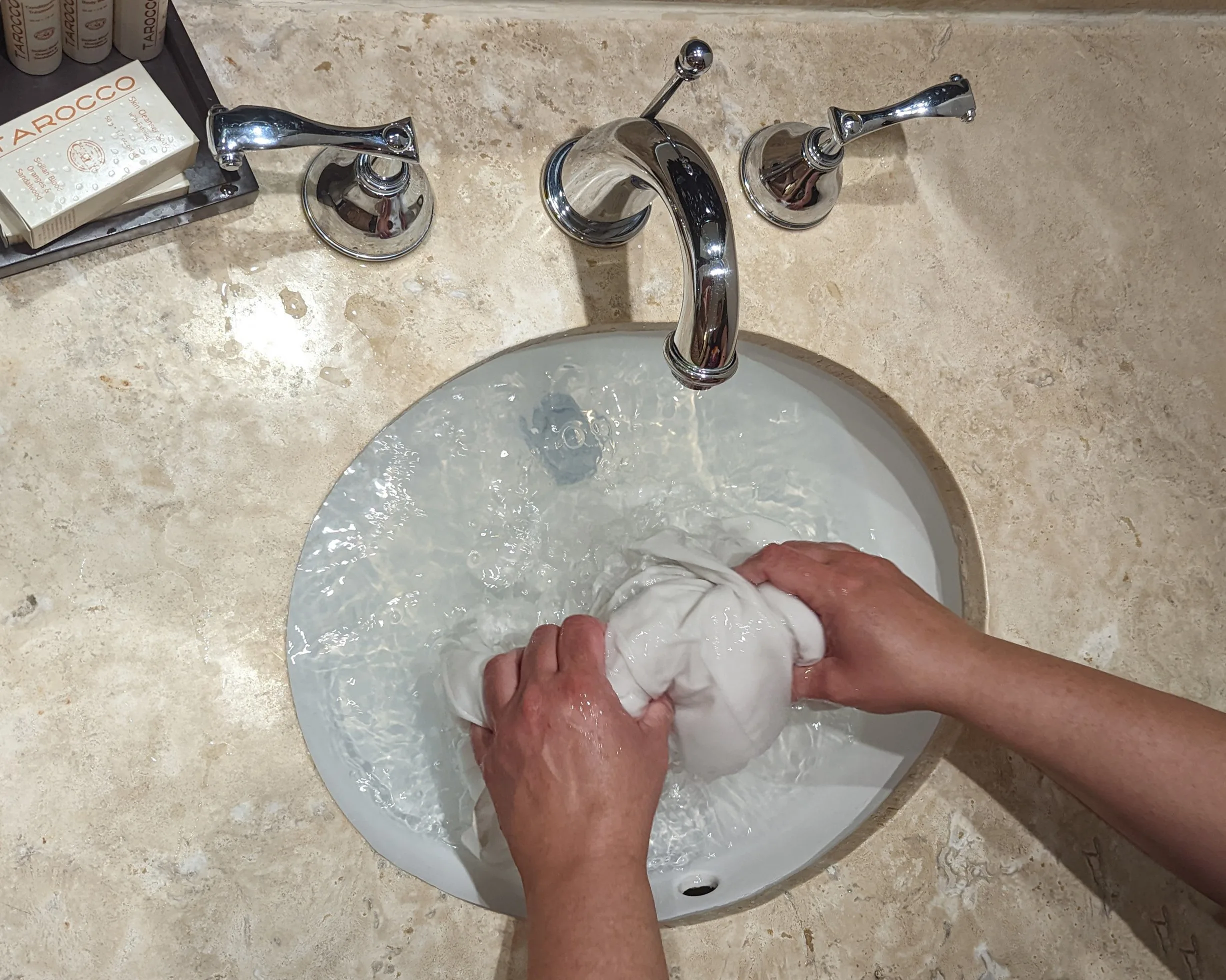 Hands scrubbing a white shirt in a hotel sink.