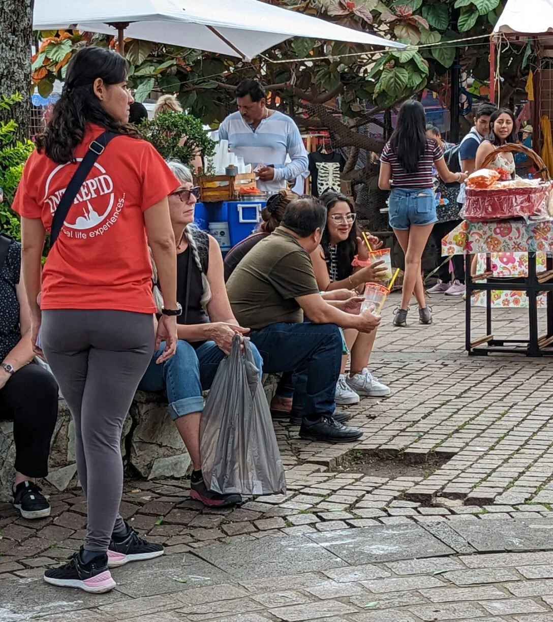 Image of people sitting on a street with market vendors surrounding them.