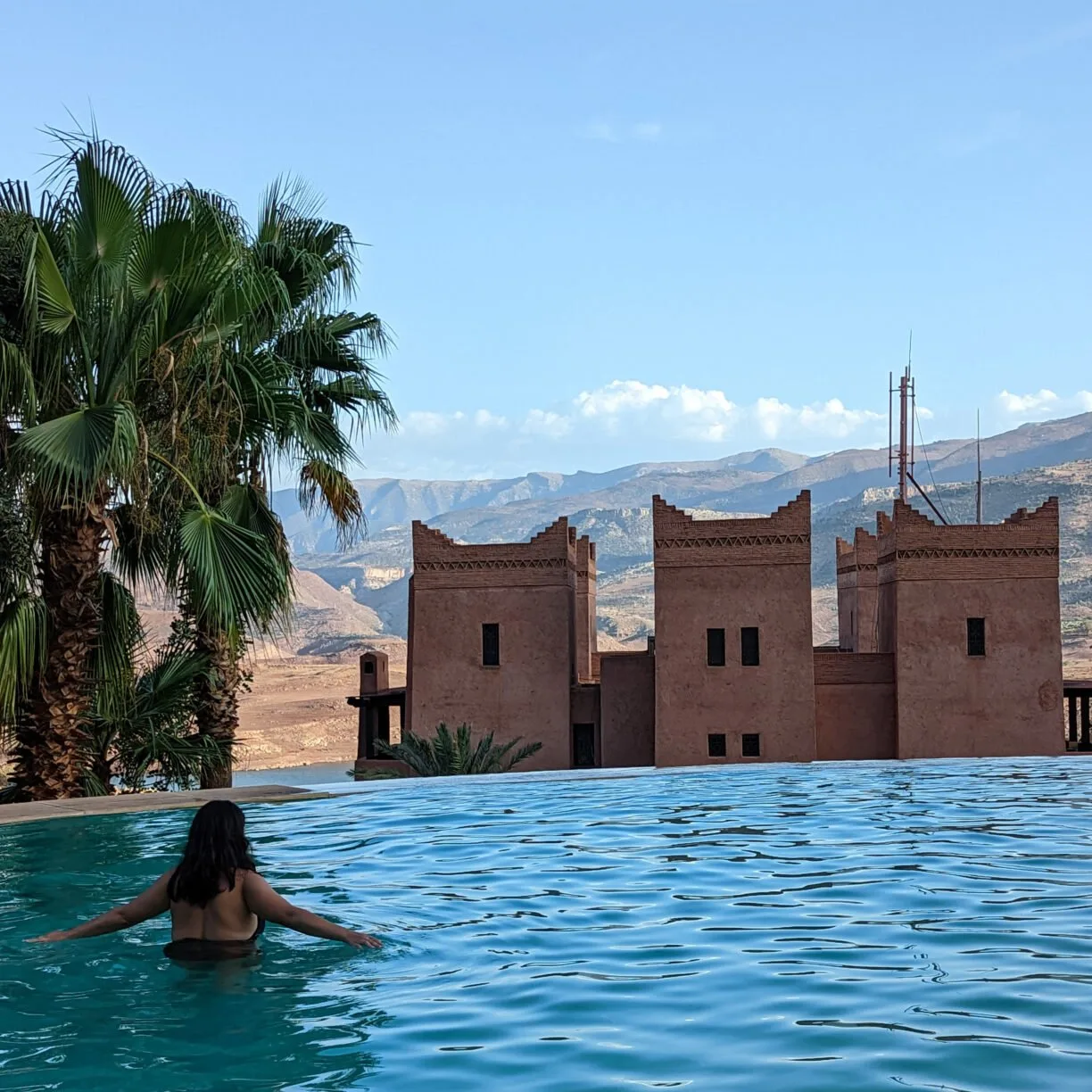 A solo female traveler wade in an infinity pool in morocco