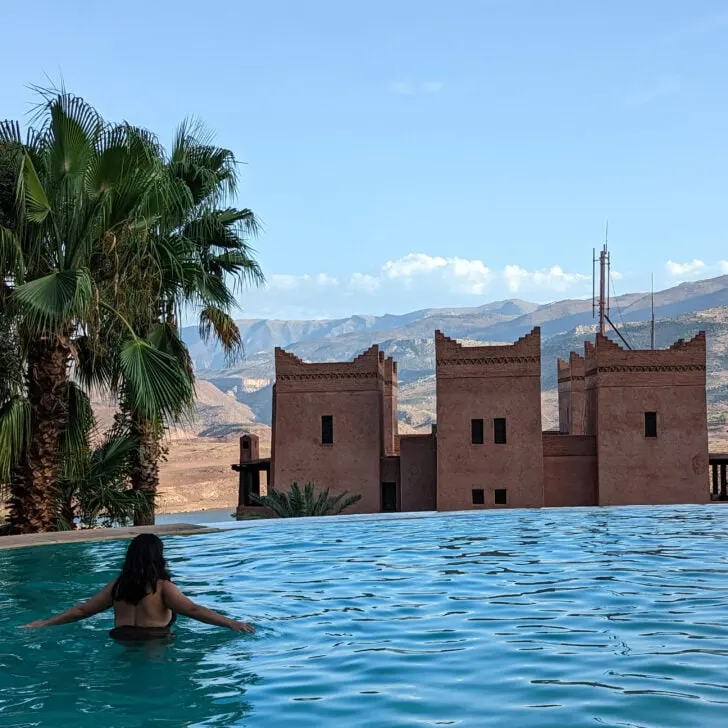 A solo female traveler wade in an infinity pool in Morocco