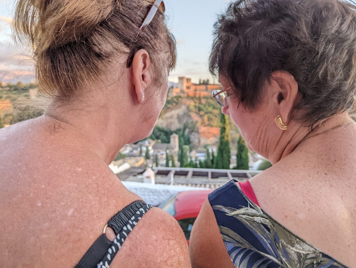 Two adult female friends share a secret while standing at an overlook viewing the alhambra in granada spain.