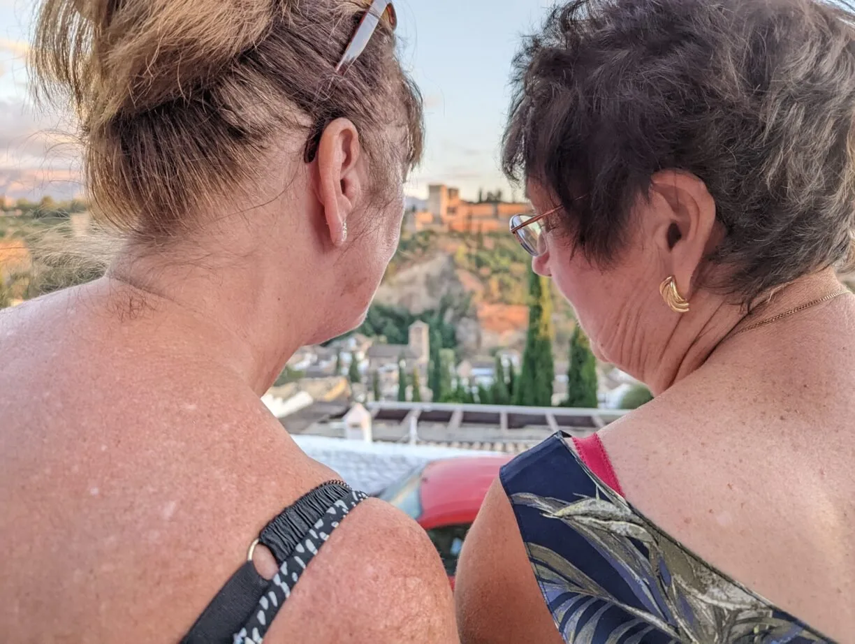 Two adult female friends share a secret while standing at an overlook viewing the alhambra in granada spain.