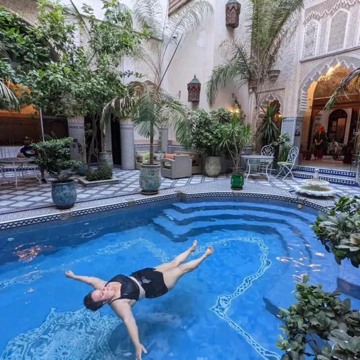 plus size traveler floats blissfully in a pool in a Moroccan riad.