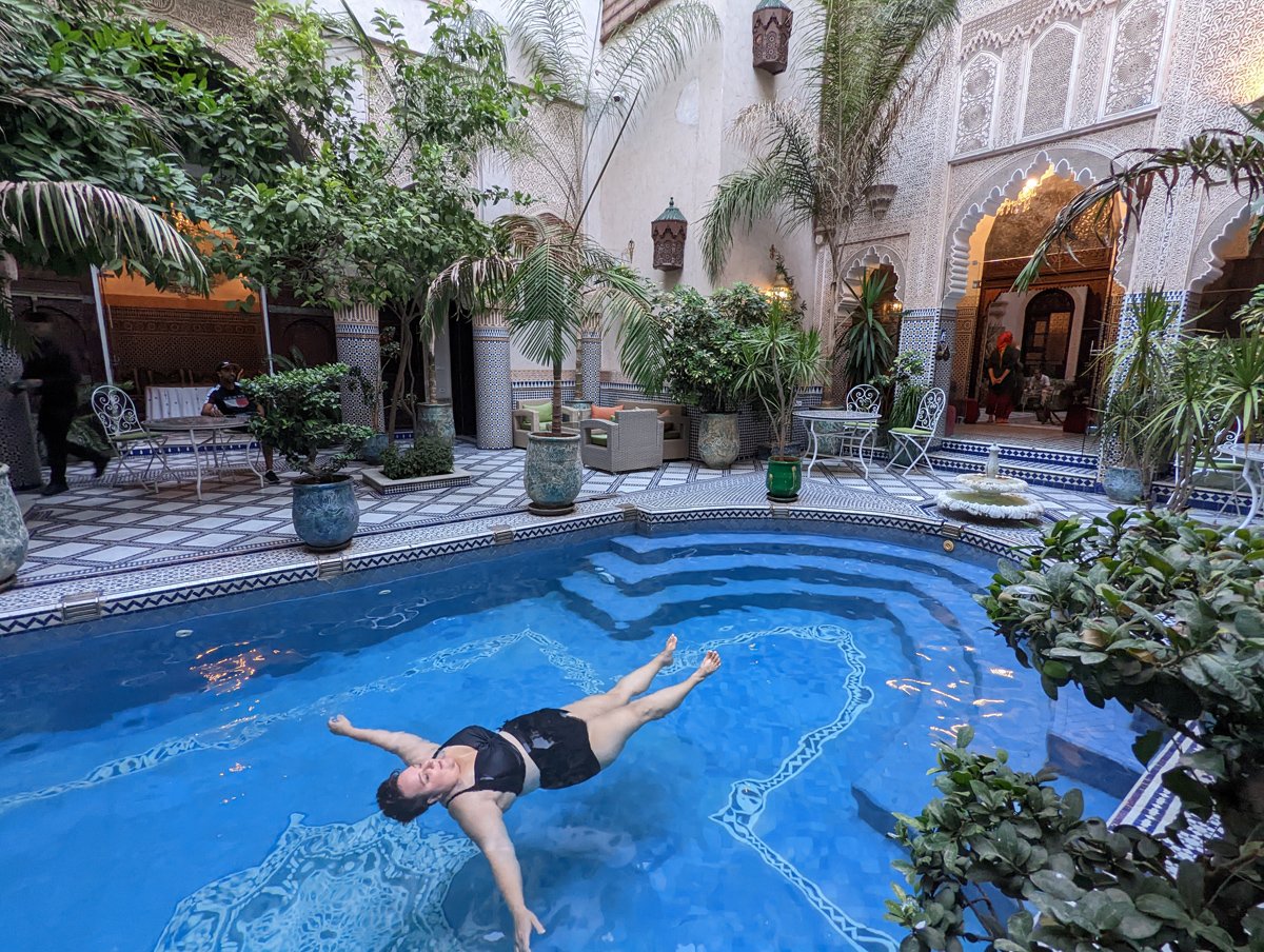 Plus size traveler floats blissfully in a pool in a moroccan riad.