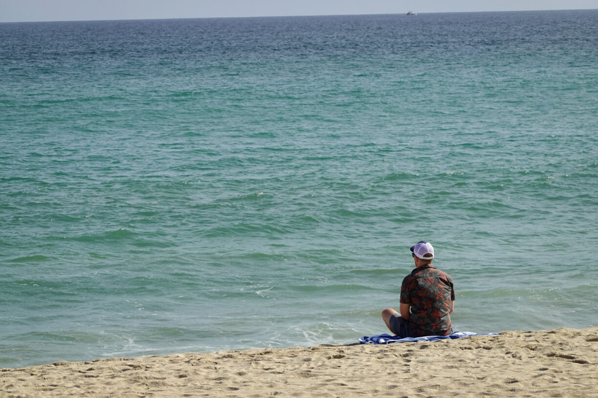 Man sitting on the beach looking at the water.