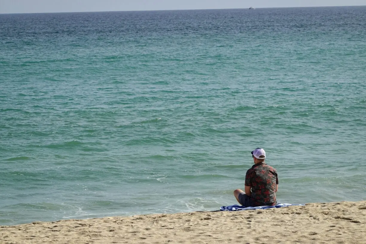 Man sitting on the beach looking at the water.