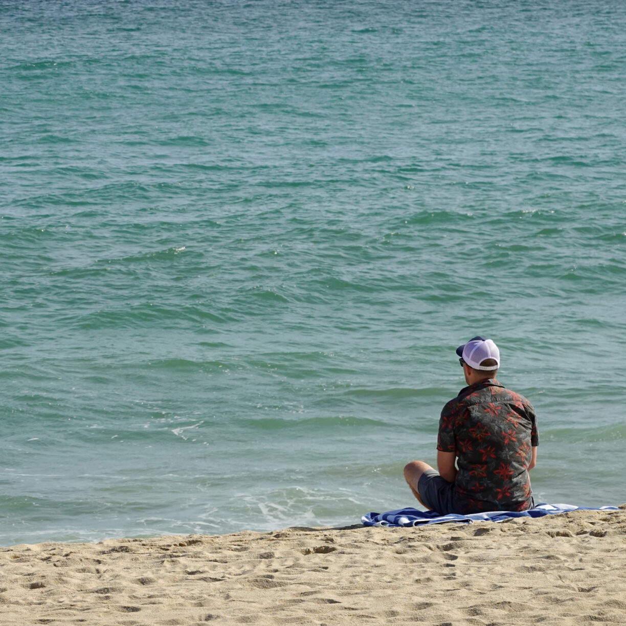 Man sitting on the beach looking at the water.