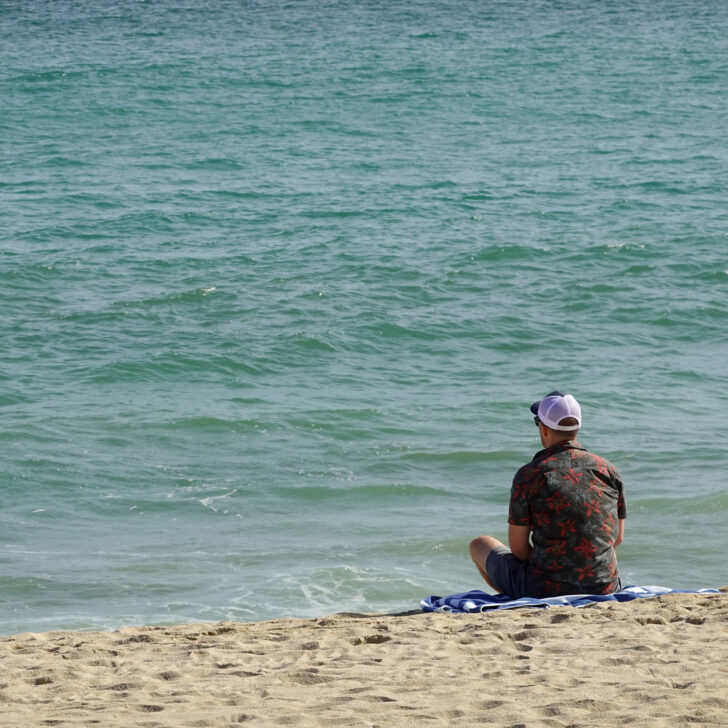 Man sitting on the beach looking at the water.