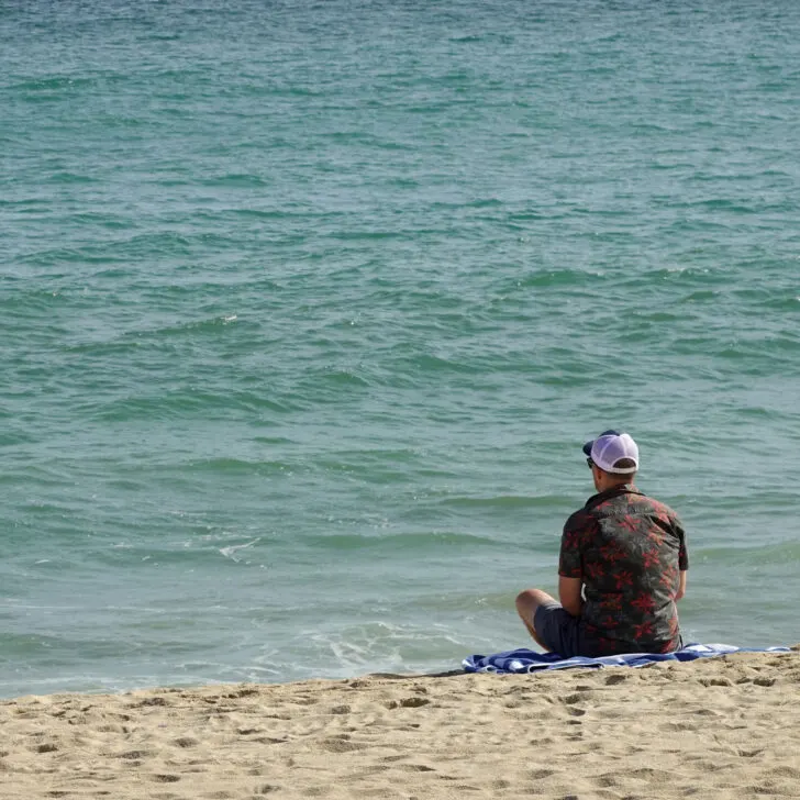 Man sitting on the beach looking at the water.